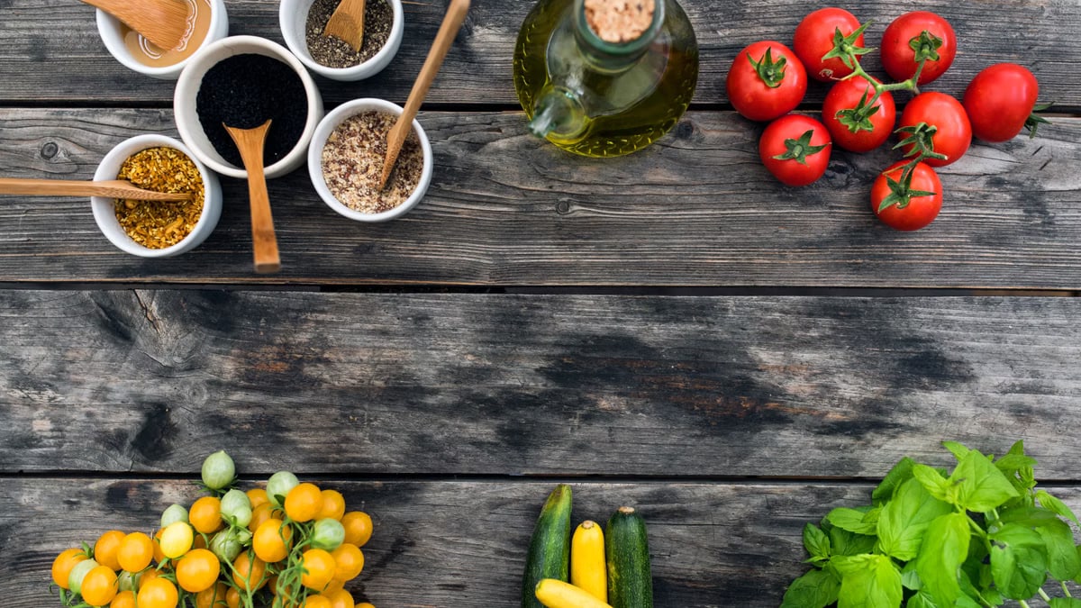 Top view of fresh vegetables and spices for salad placed on wooden table in daytime